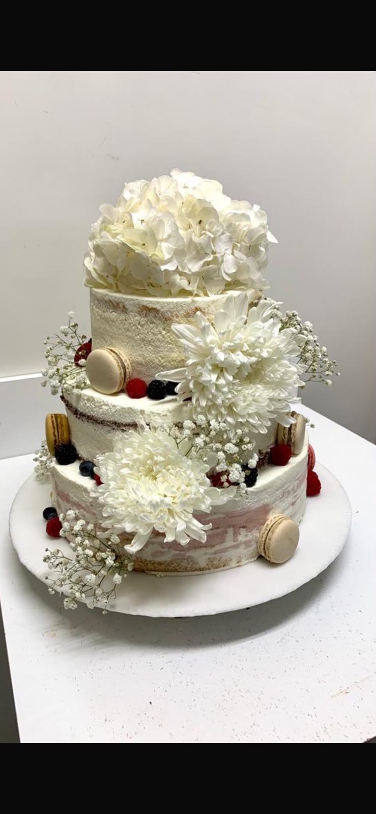 Dreistöckige Festtagstorte mit weißen Blüten, Beeren und Macarons
